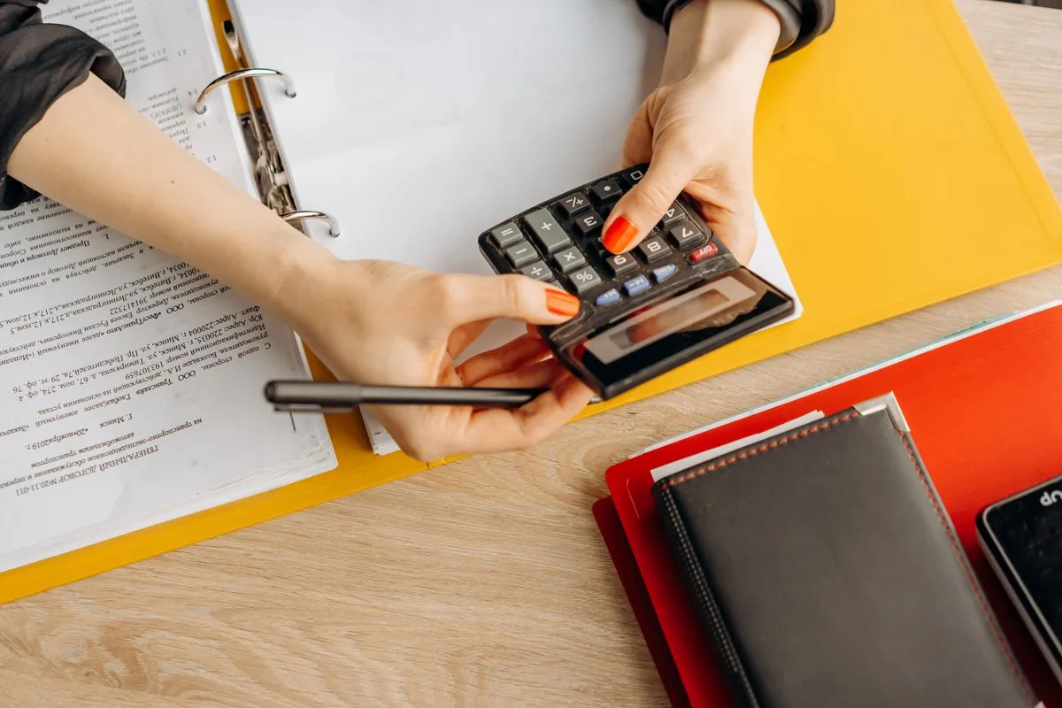 Hands using a calculator over a desk with documents and folders, organizing accounts payable and receivable