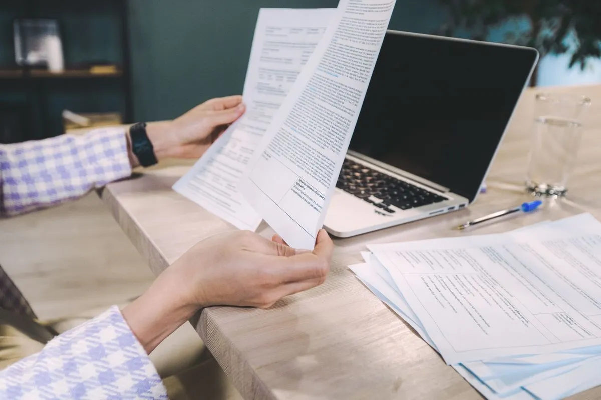 Hands reviewing printed documents next to a laptop on the desk